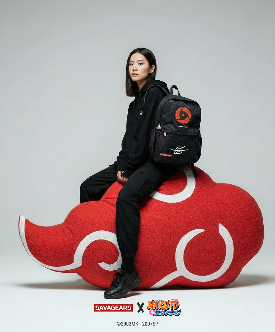 SAVAGEARS X NARUTO SHIPPUDEN - Collaboration Announcement | SAVAGEARS® Official Online Store Asian female model wearing a black hoodie and black pants sits on a large red Akatsuki cloud pillow while carrying the official SAVAGEARS X NARUTO SHIPPUDEN Itachi backpack. The black backpack features the red Mangekyō Sharingan symbol, the Hidden Leaf Village logo, red SAVAGEEARS woven label, and Akatsuki cloud zipper pulls. Studio background in light gray, with SAVAGEEARS × Naruto Shippuden collaboration logos displayed at the bottom.